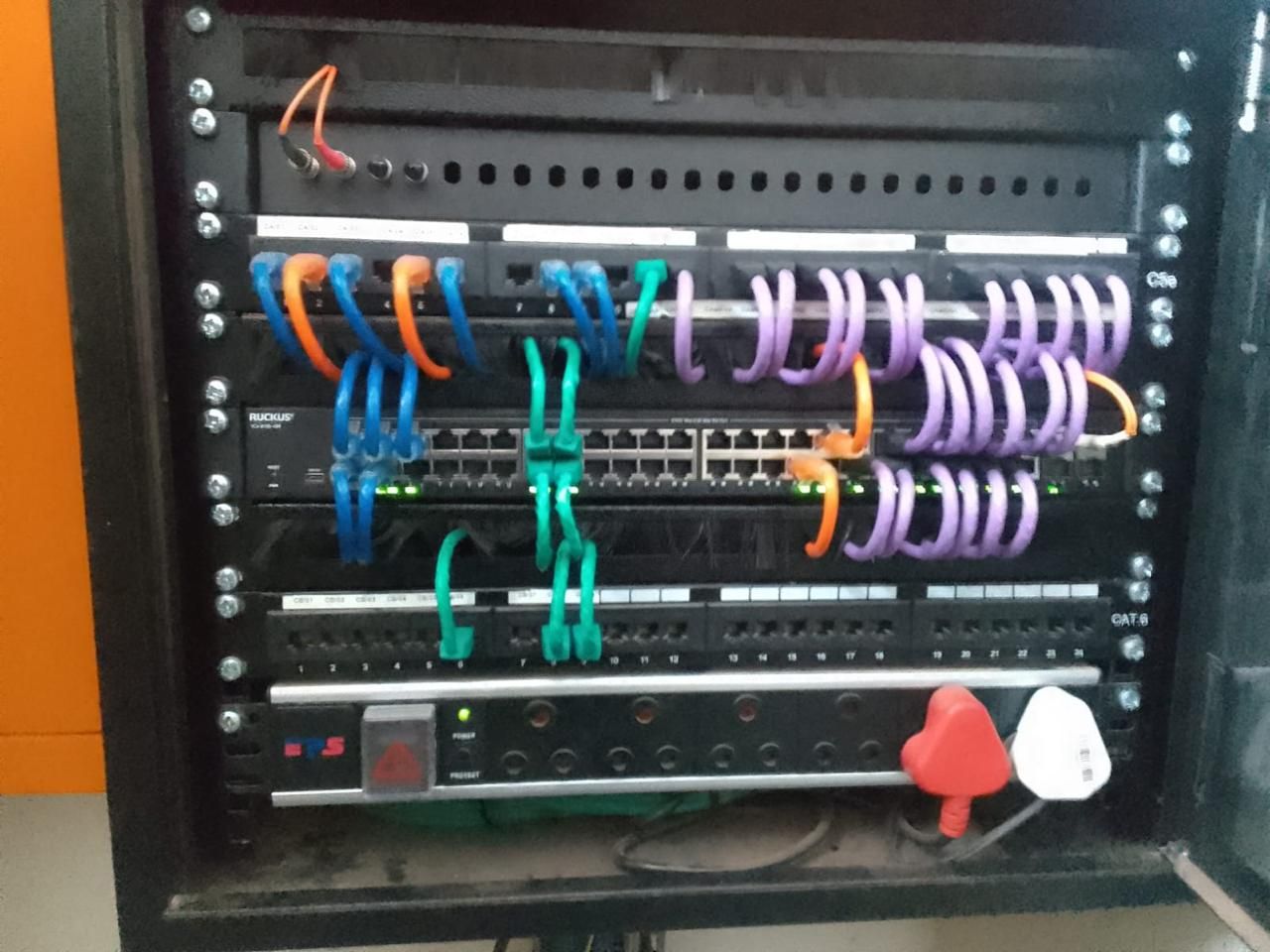 A wall cabinet with a Ruckus switch, Cat6 patch panels and a power strip